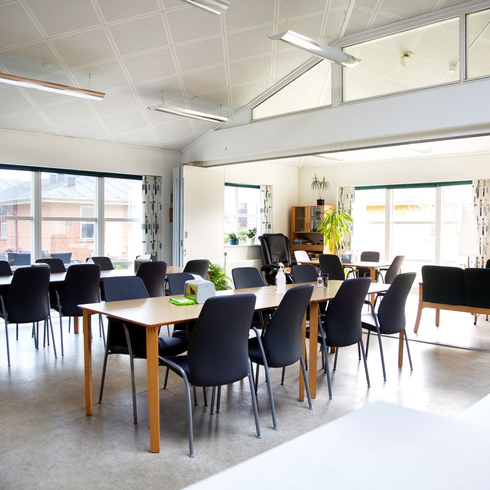 Fællesrum med spiseborde og stole, samt et opdelt rum med sofaer og lænestole man kan lukke af til.