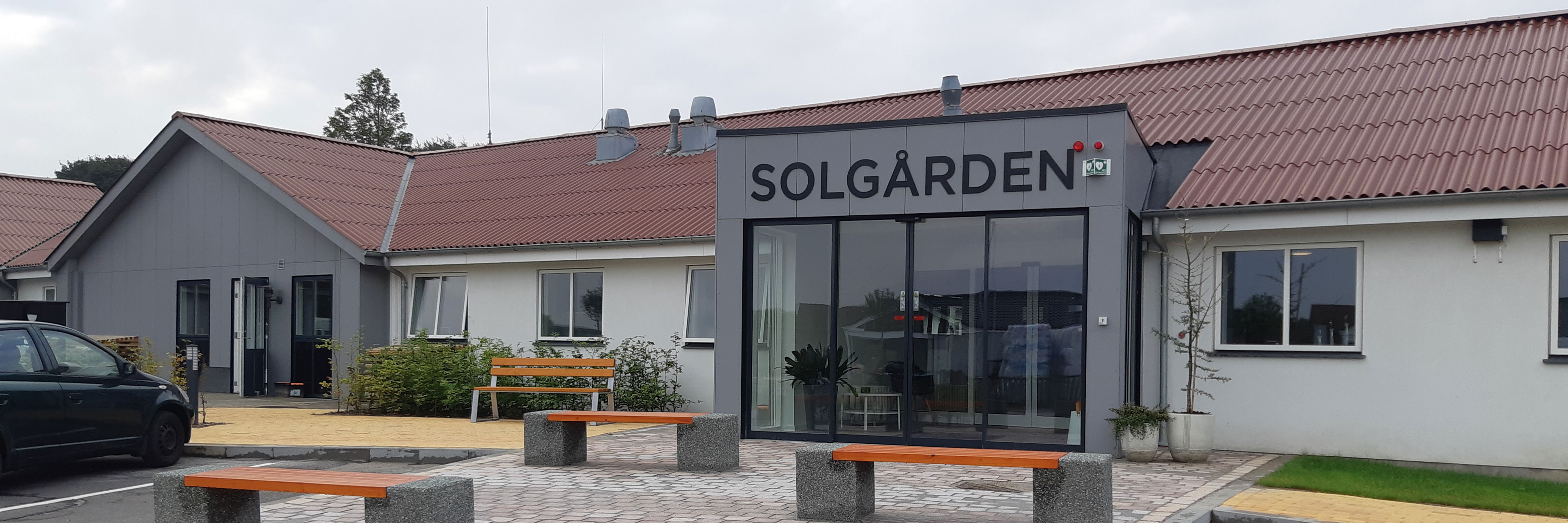 Forsiden af Solgården, grå fliser og nogle bænke i beton med træsæder