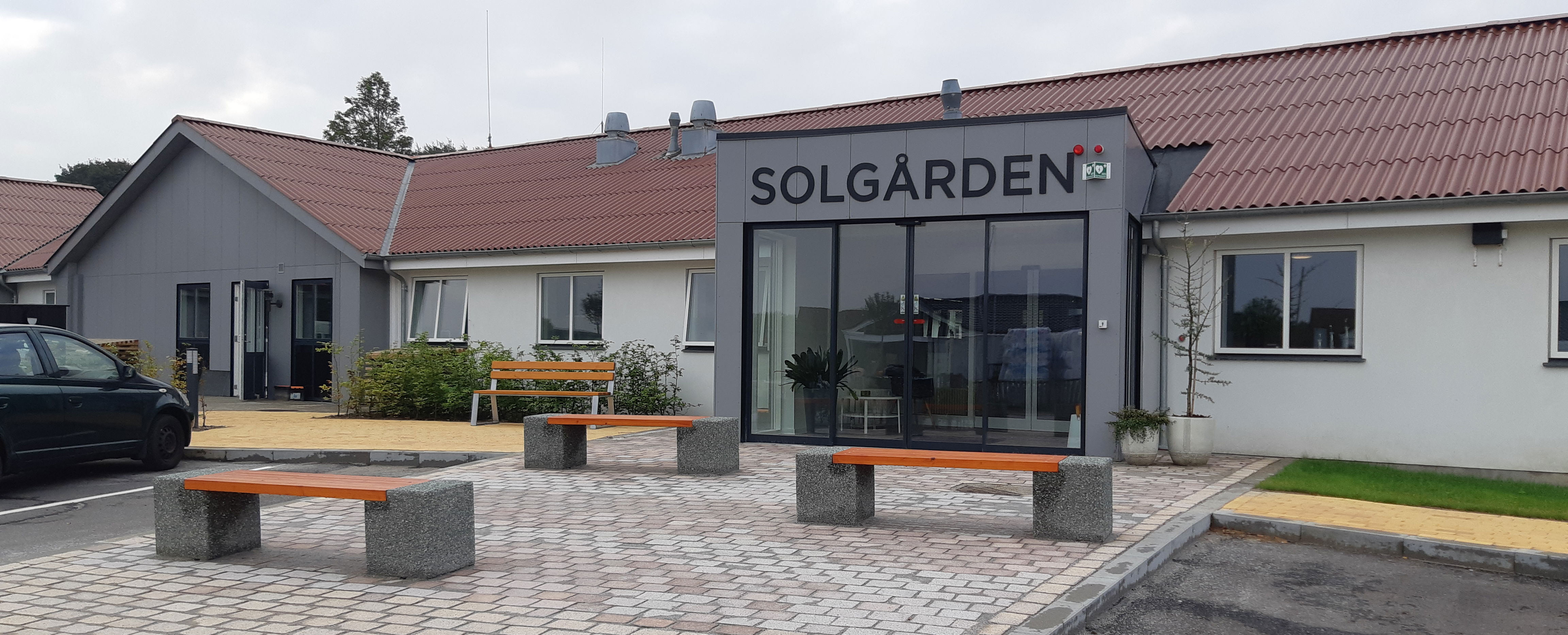 Forsiden af Solgården, grå fliser og nogle bænke i beton med træsæder