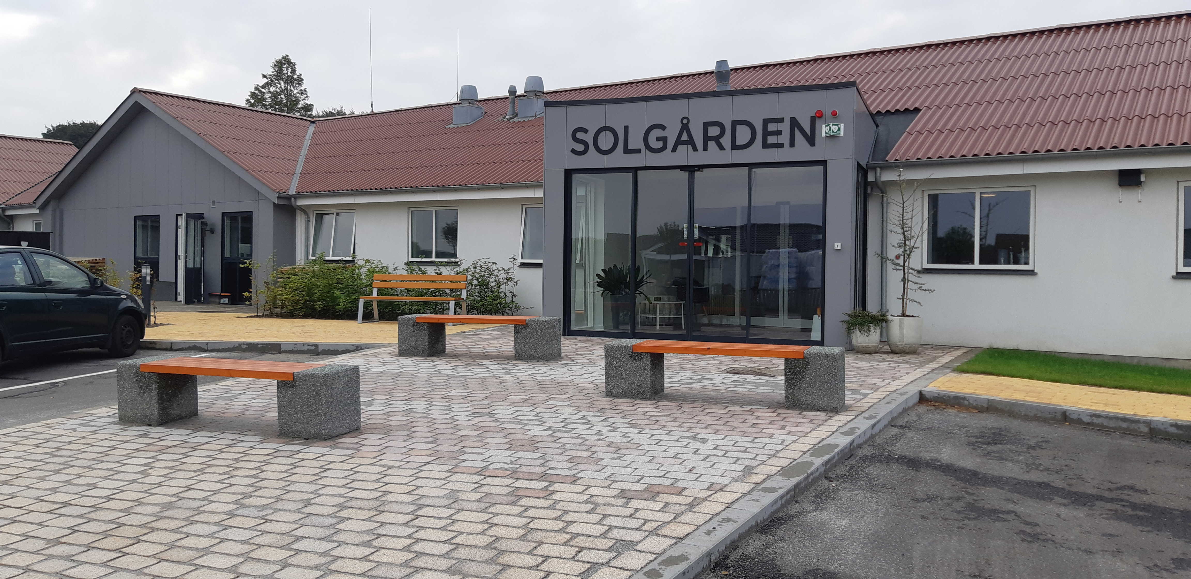 Forsiden af Solgården, grå fliser og nogle bænke i beton med træsæder