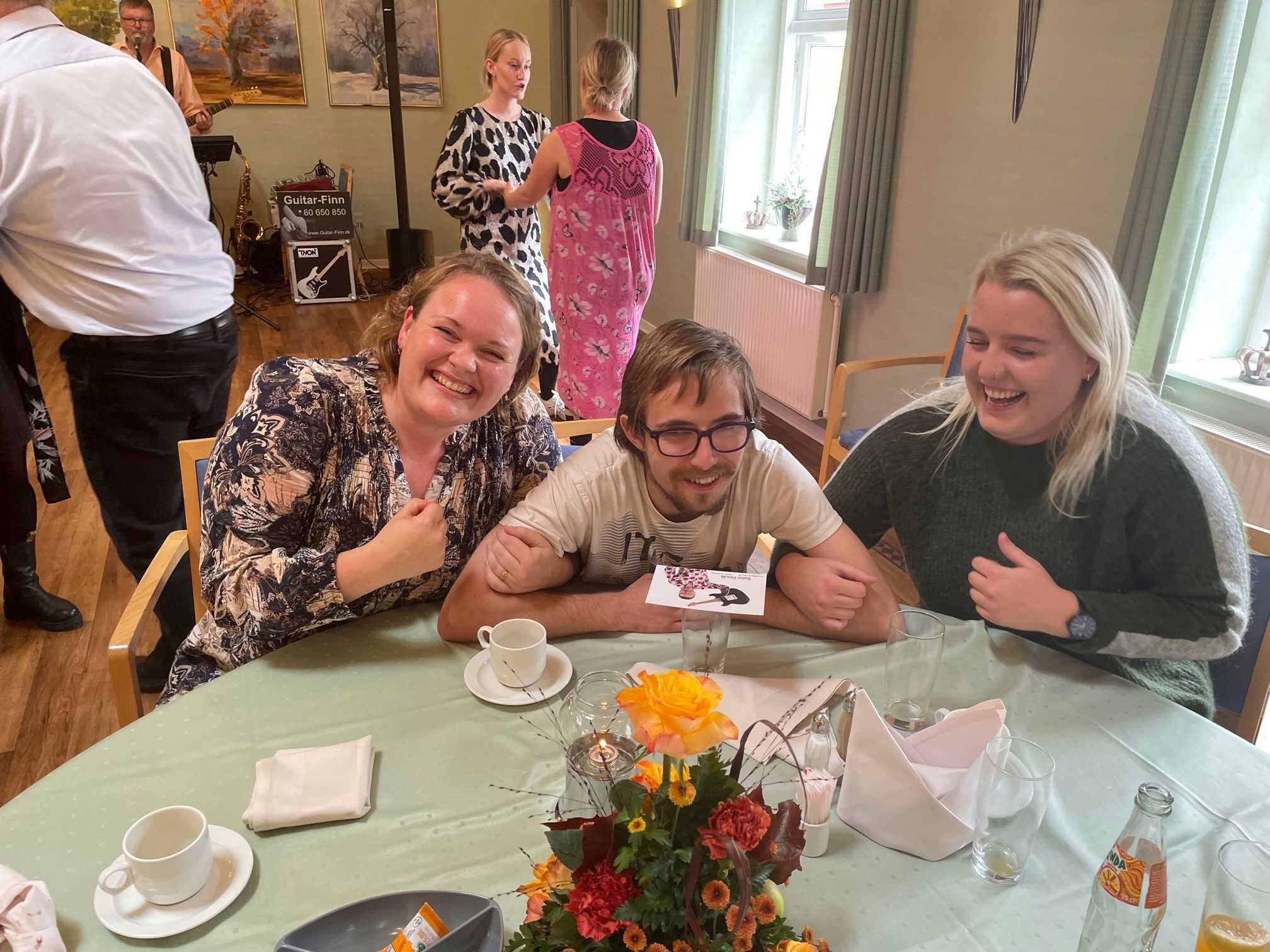 # glade gæster der smiler til cameraet, i baggrunden kan man se nogle der dansker til musikken