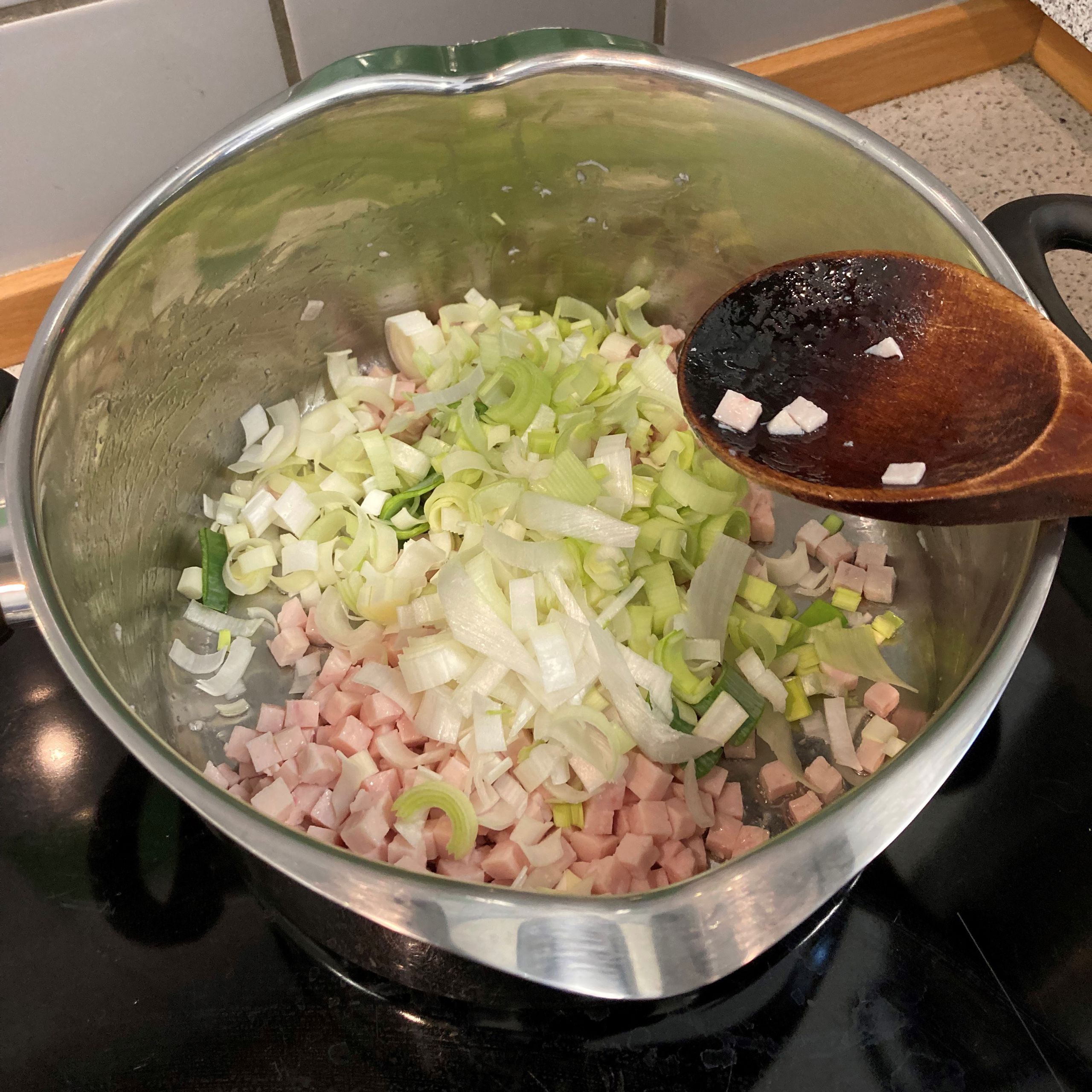 Nede i grydes ses kødet og porrerne, der bliver rørt i det med en grydeske af træ.