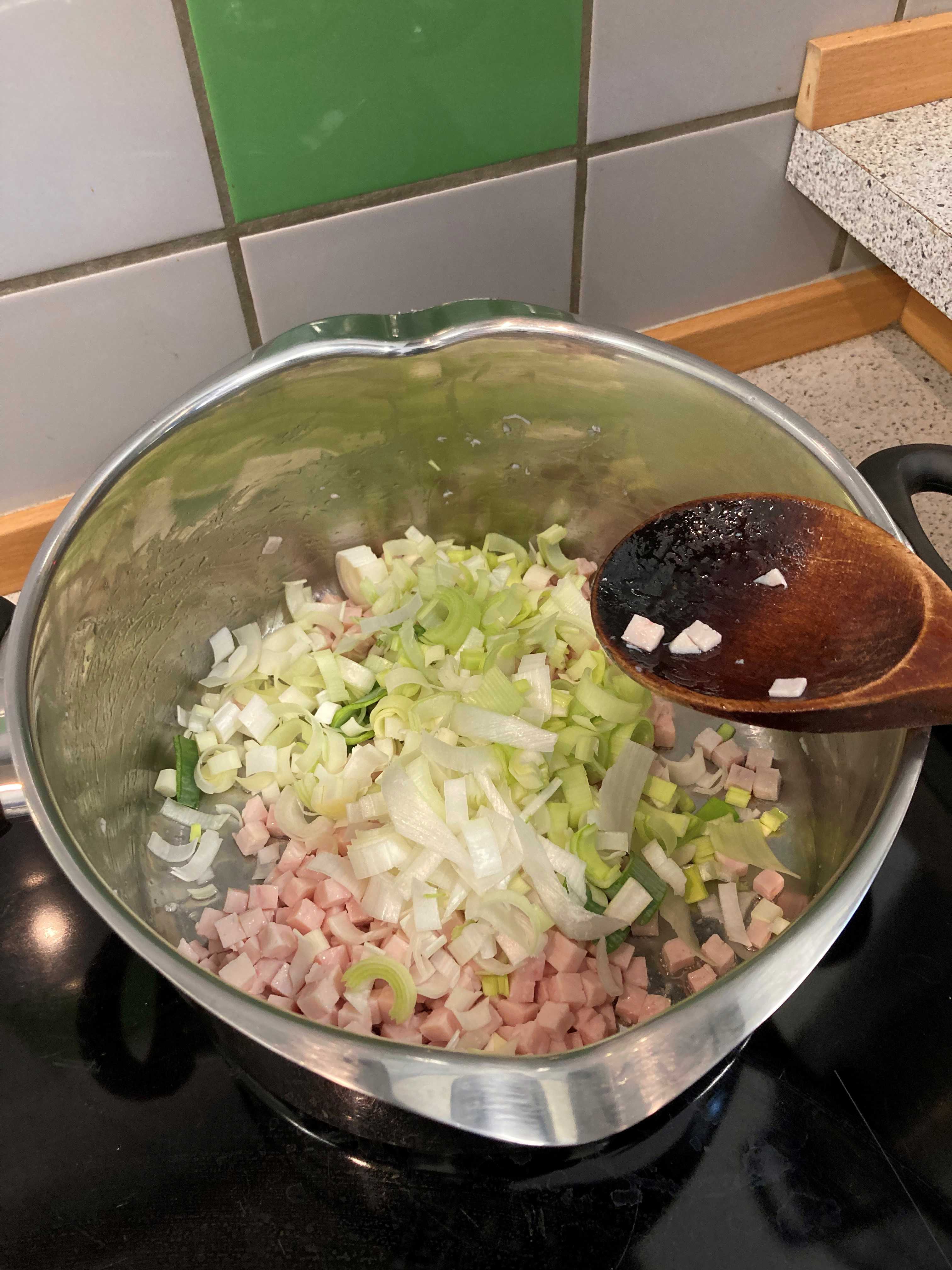 Nede i grydes ses kødet og porrerne, der bliver rørt i det med en grydeske af træ.