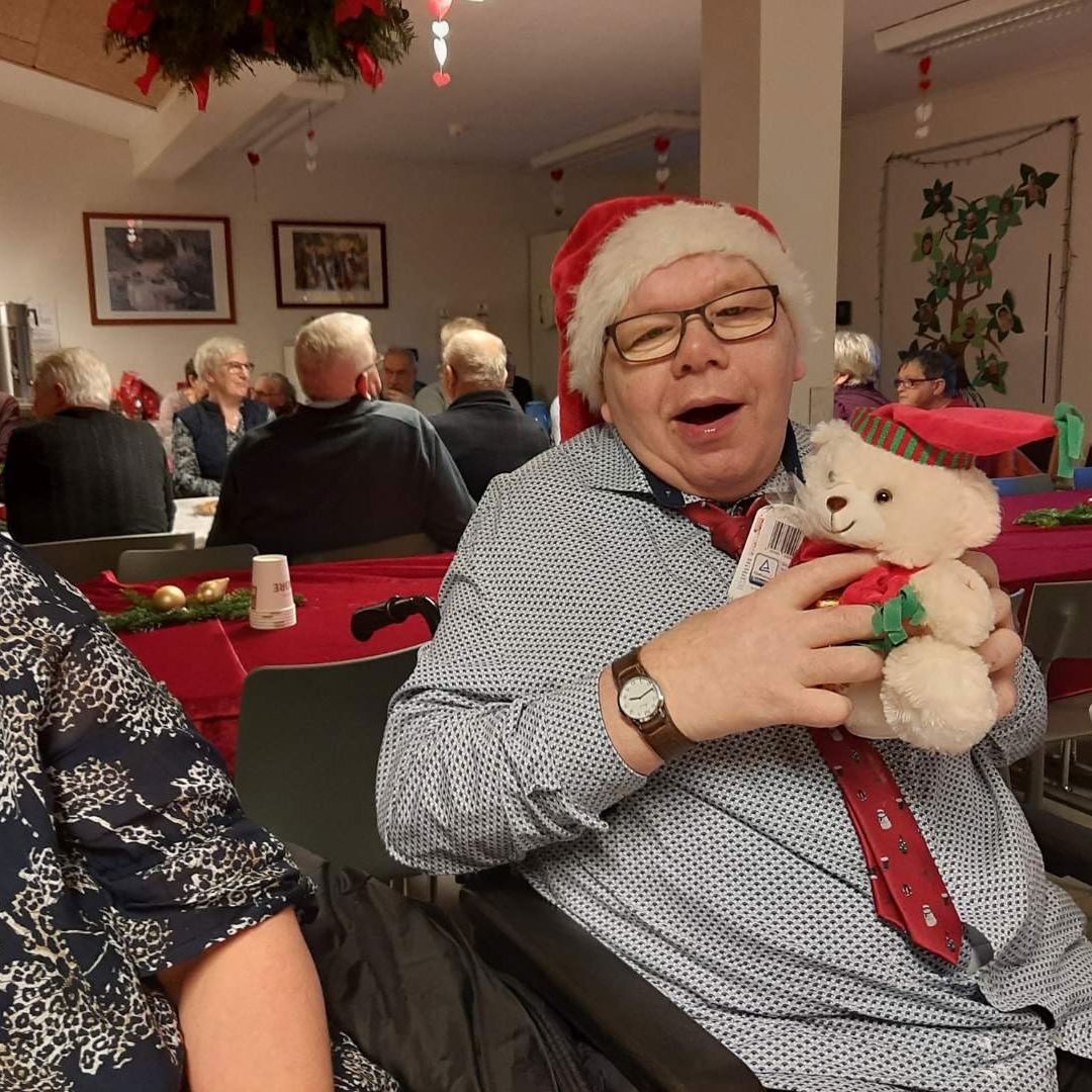 Borger sidder foran et juledækket bord. Borger har en nissehue på, og sidder med en julebamse i favnen.