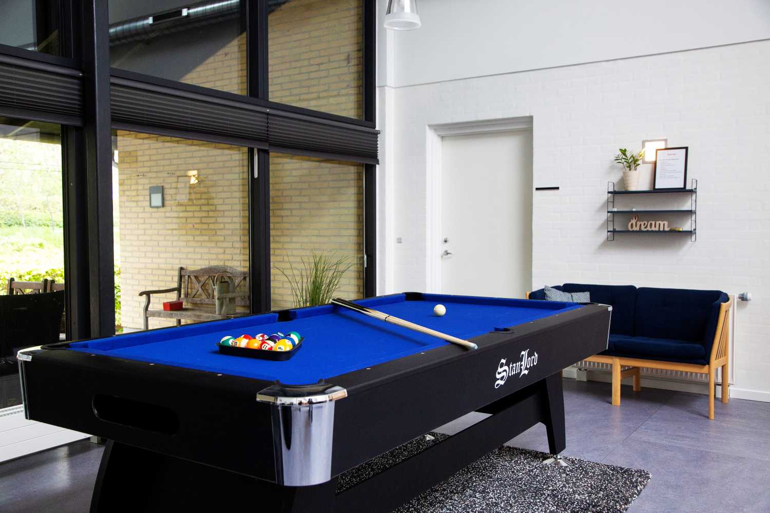 Billardbord sorte med blå dug ovenpå ligger billardkuglerne og to køer. det står op af et stort vinduesparti