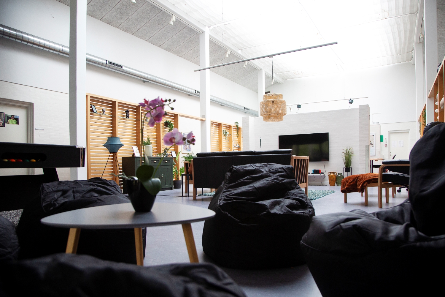 Hjørne i fællesrummet med fire sækkestole rundt om et lille sofabord i baggrunden er sofaer og tv på væggen