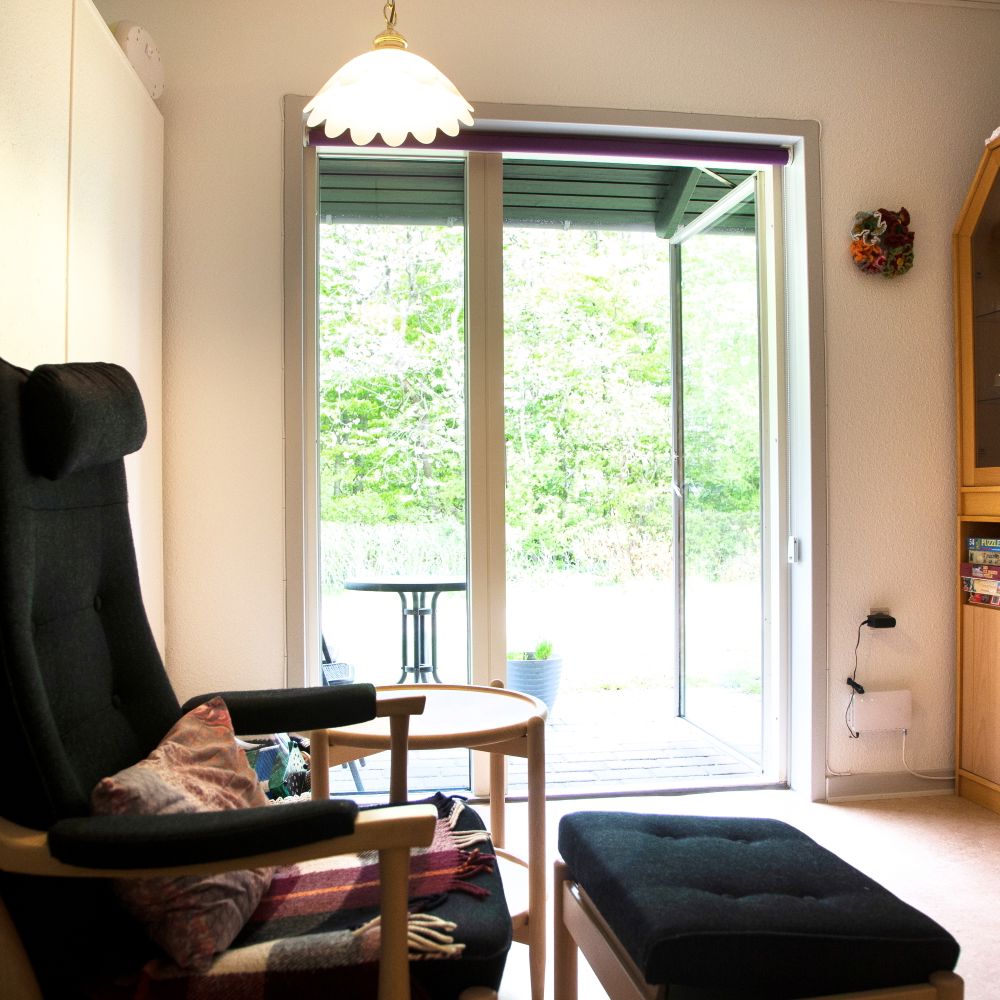 Foran i billedet står der en lænestol med skammel og der står en reol.