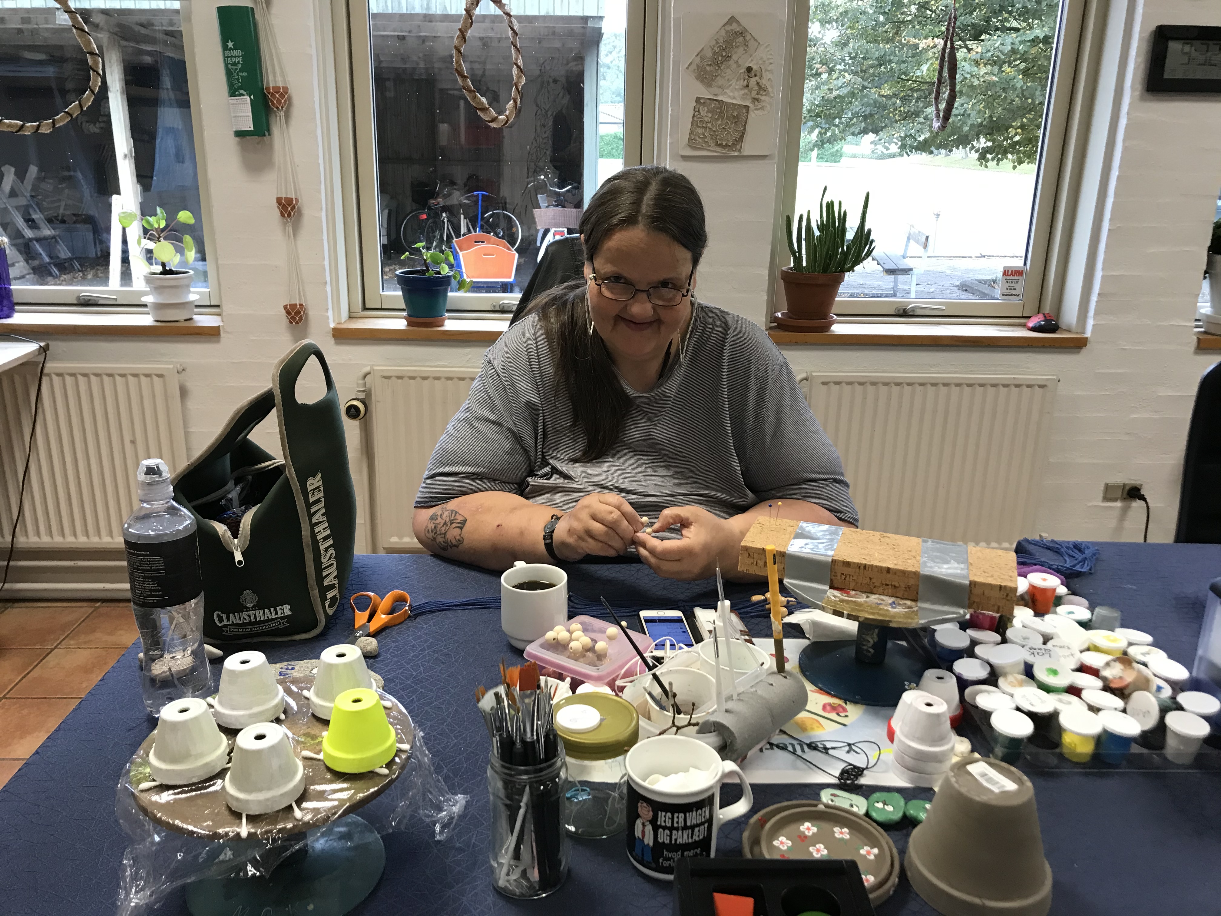 Borger sidder og maler urtepotter foran på bordet er der forskellige størrelser urtepotter og farver malinger 