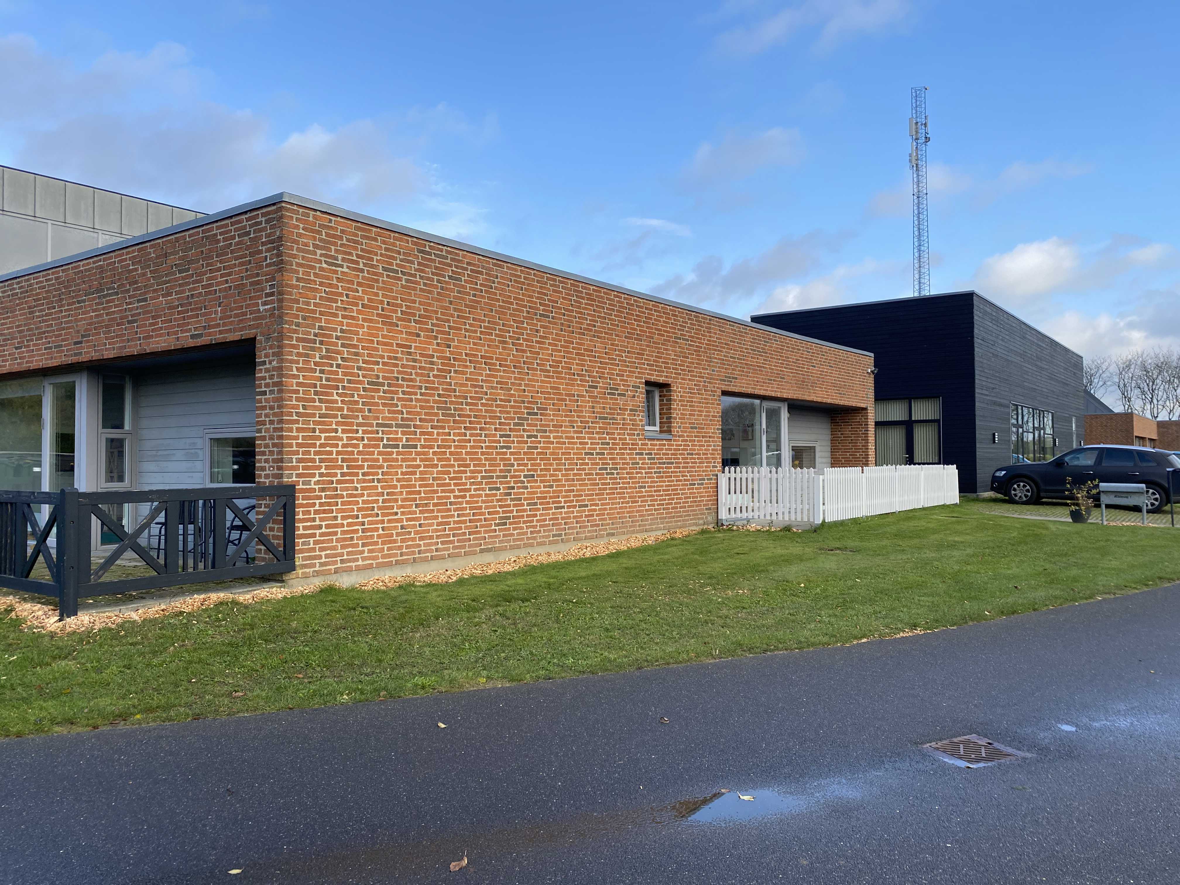 Æblevej 1 udvendigt, der er asfalteret vej udenom. Terrassen bagved Æblevej 1 er indhegnet med et sort lavt stakit. Der er en indhegnet terrasse med et hvidt lavt stakit foran Æblevej 1.