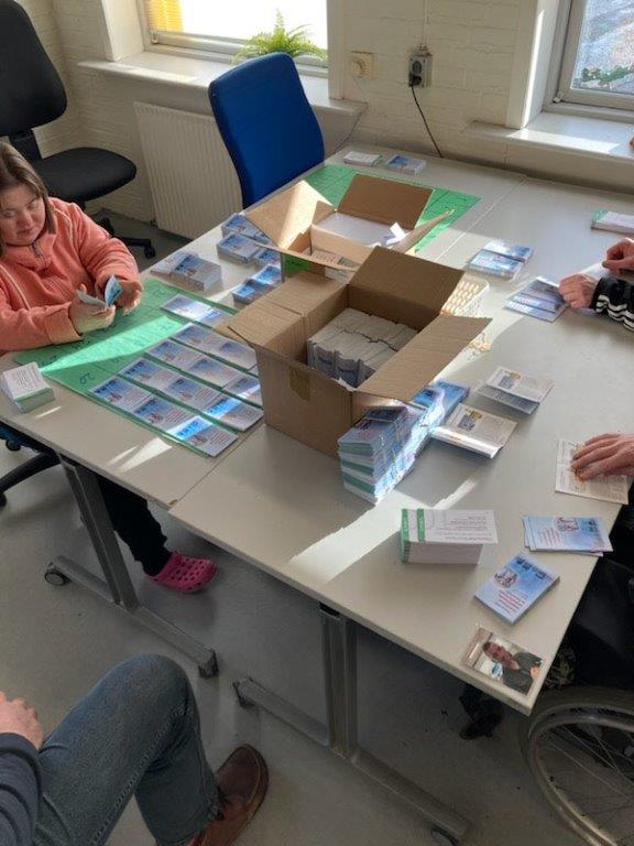 Borger sidder og pakker forskellige kort, de ligger alle i bunker og de skal derefter pakkes pakkes i en stor kasse inden de skal sendes.