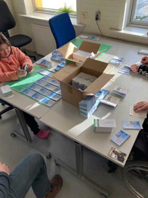 Borger sidder og pakker forskellige kort, de ligger alle i bunker og de skal derefter pakkes pakkes i en stor kasse inden de skal sendes.