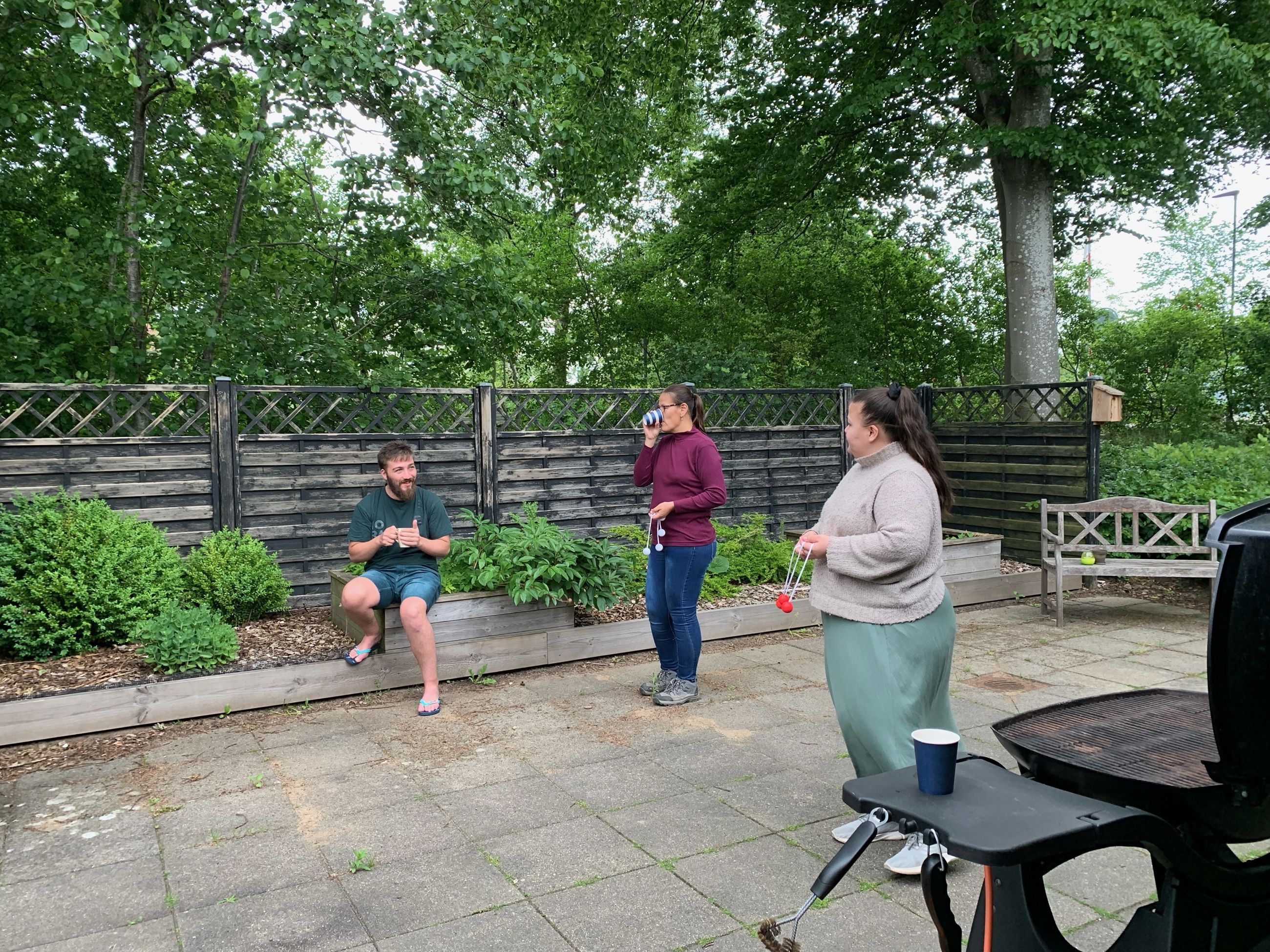 2 kvinder spiller stigegolf, i baggrunden sidder der en mand og følger med mens han drikker en kop kaffe.