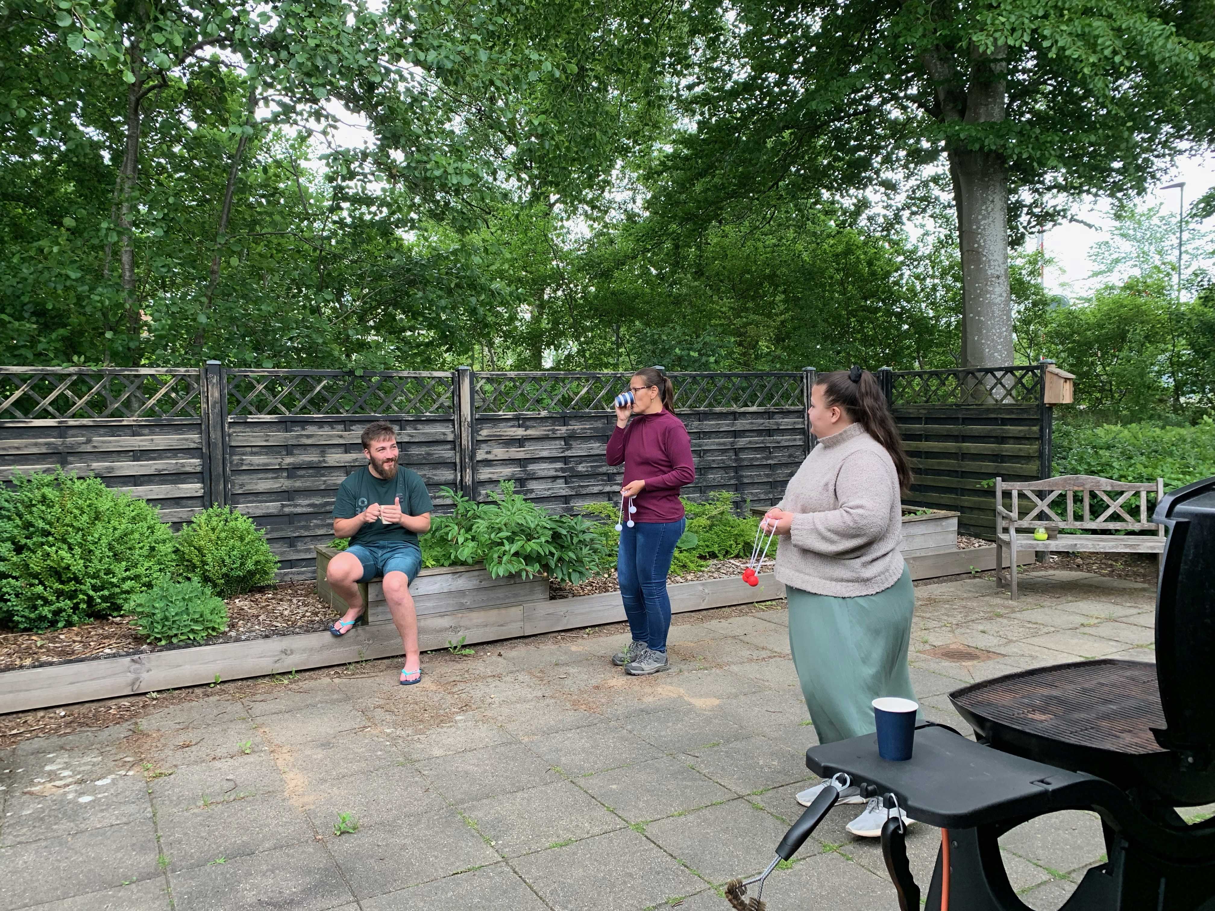 2 kvinder spiller stigegolf, i baggrunden sidder der en mand og følger med mens han drikker en kop kaffe.