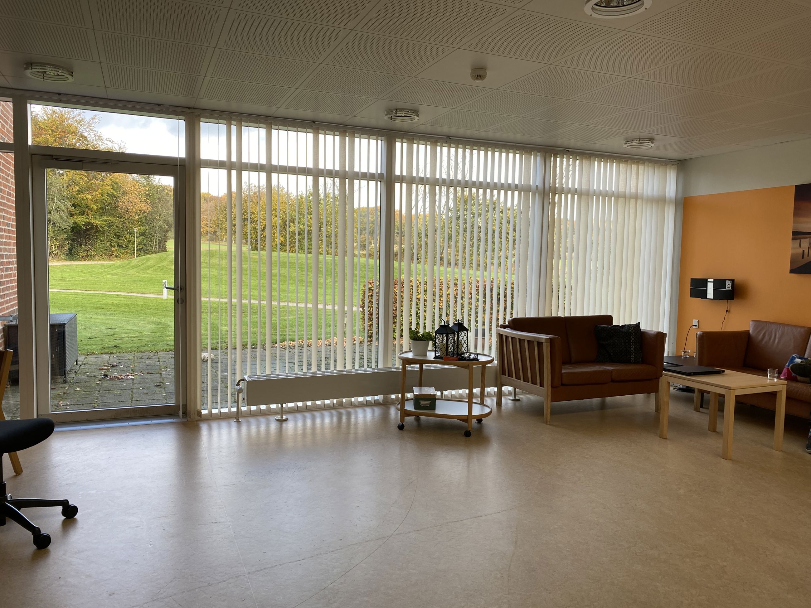 Opholdsstuen på Æblevej 1 er der to brune læder sofaer og et lille firkantet bord. Den ene væg i stuen er malet orange. Gulvet er lysebrunt.