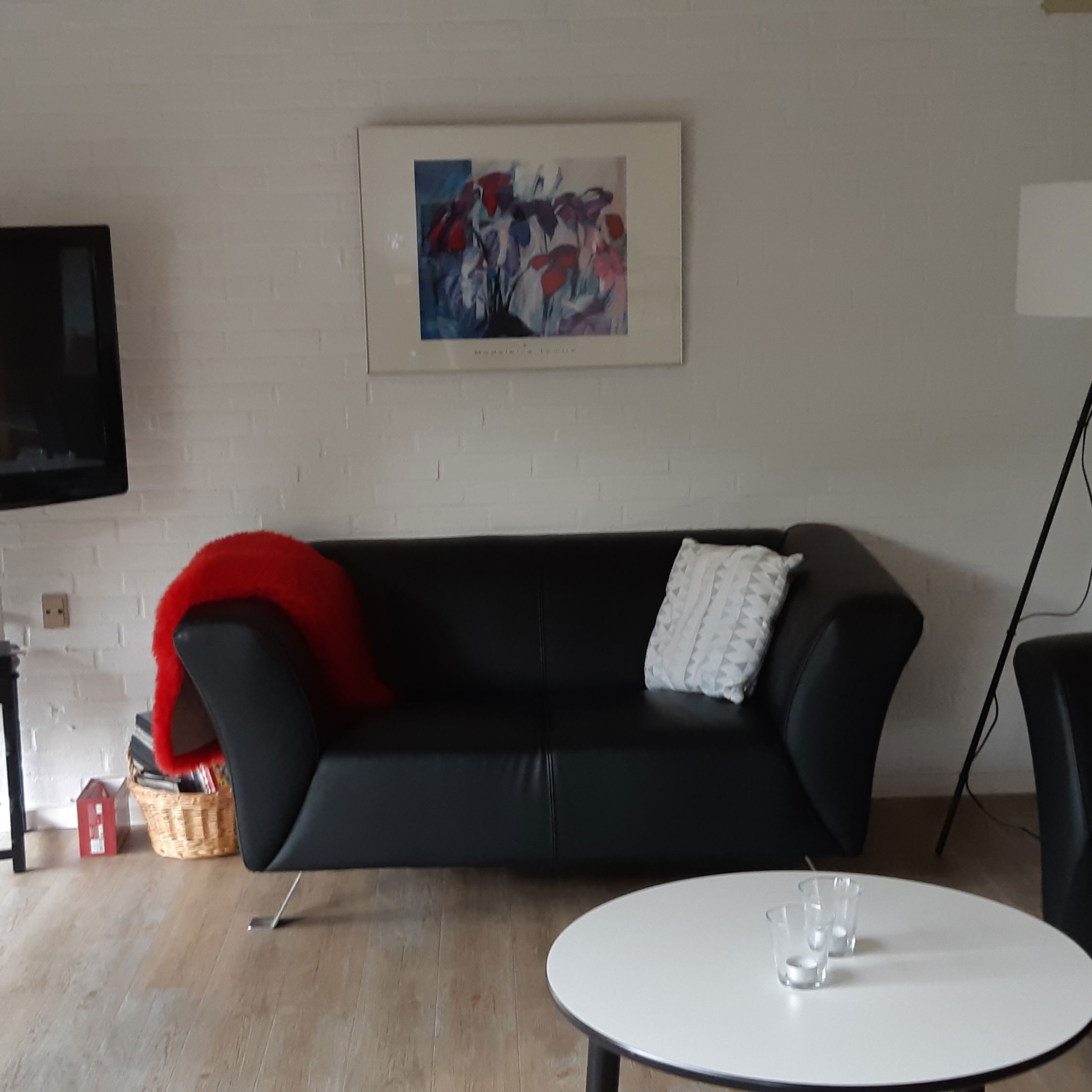 Opholdsstue med to lædersofaer, et rundt bord og et tv. I hjærnet er der er høj standerlampe med hvid lampeskærm.