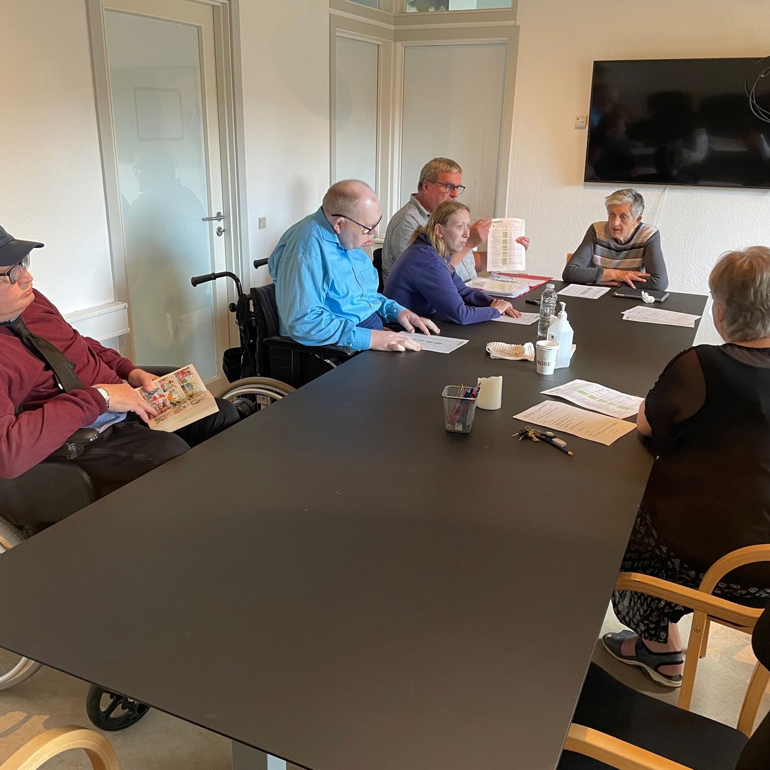 Et langt bord hvor der sidder syv personer omkring som deltager i afdelingsmøde.