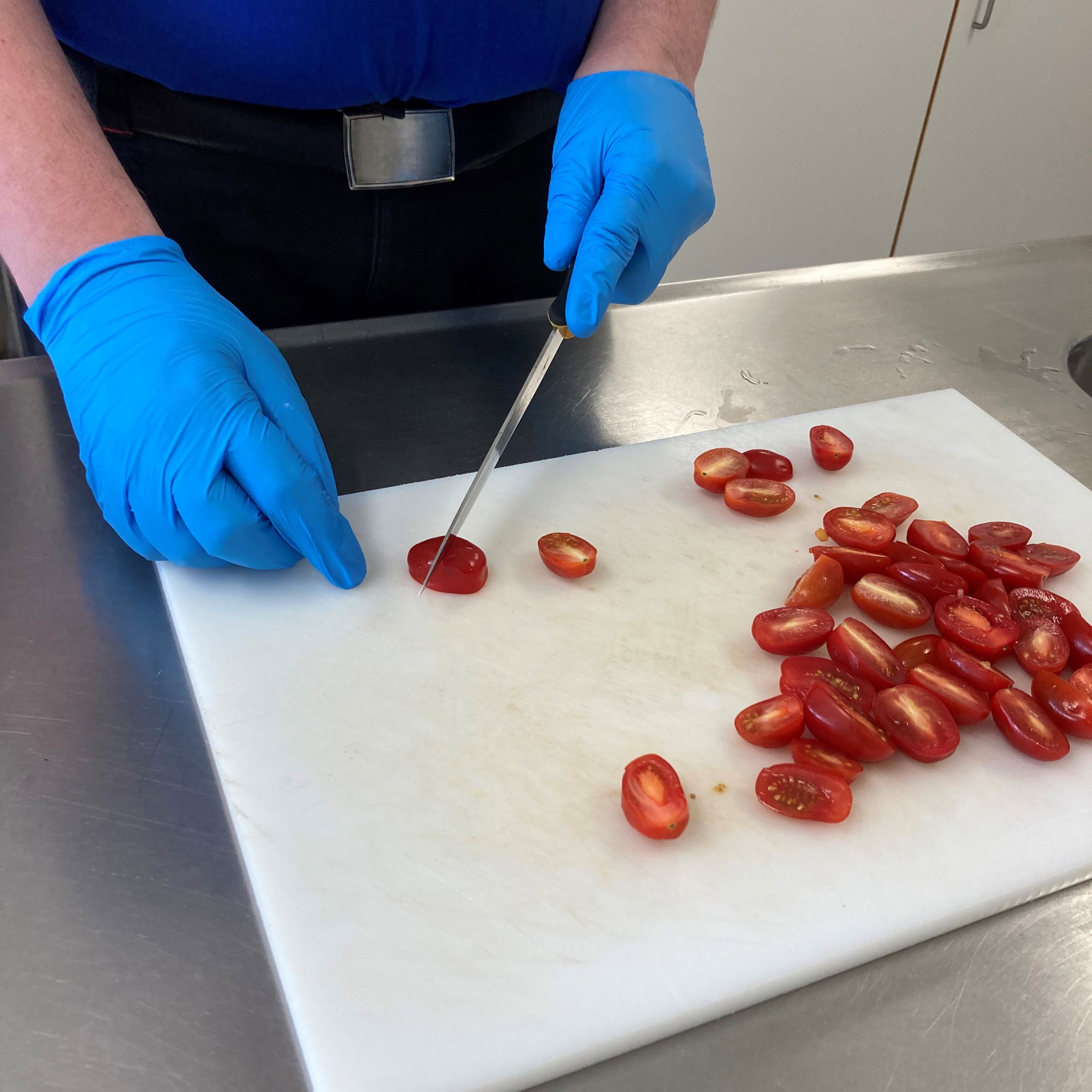 En borger skærer cherrytomater i halve på et hvidt skærebræt.