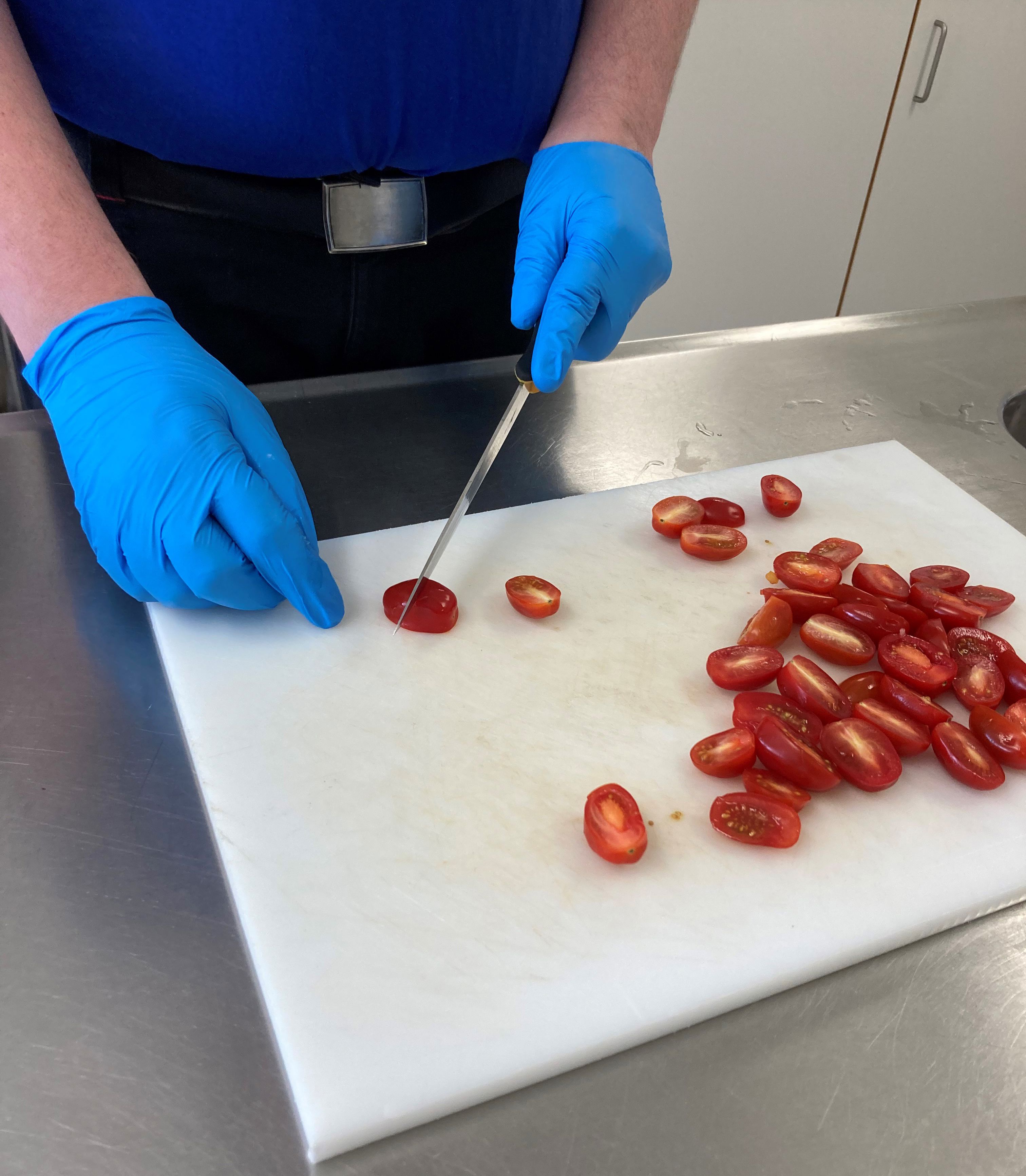 En borger skærer cherrytomater i halve på et hvidt skærebræt.