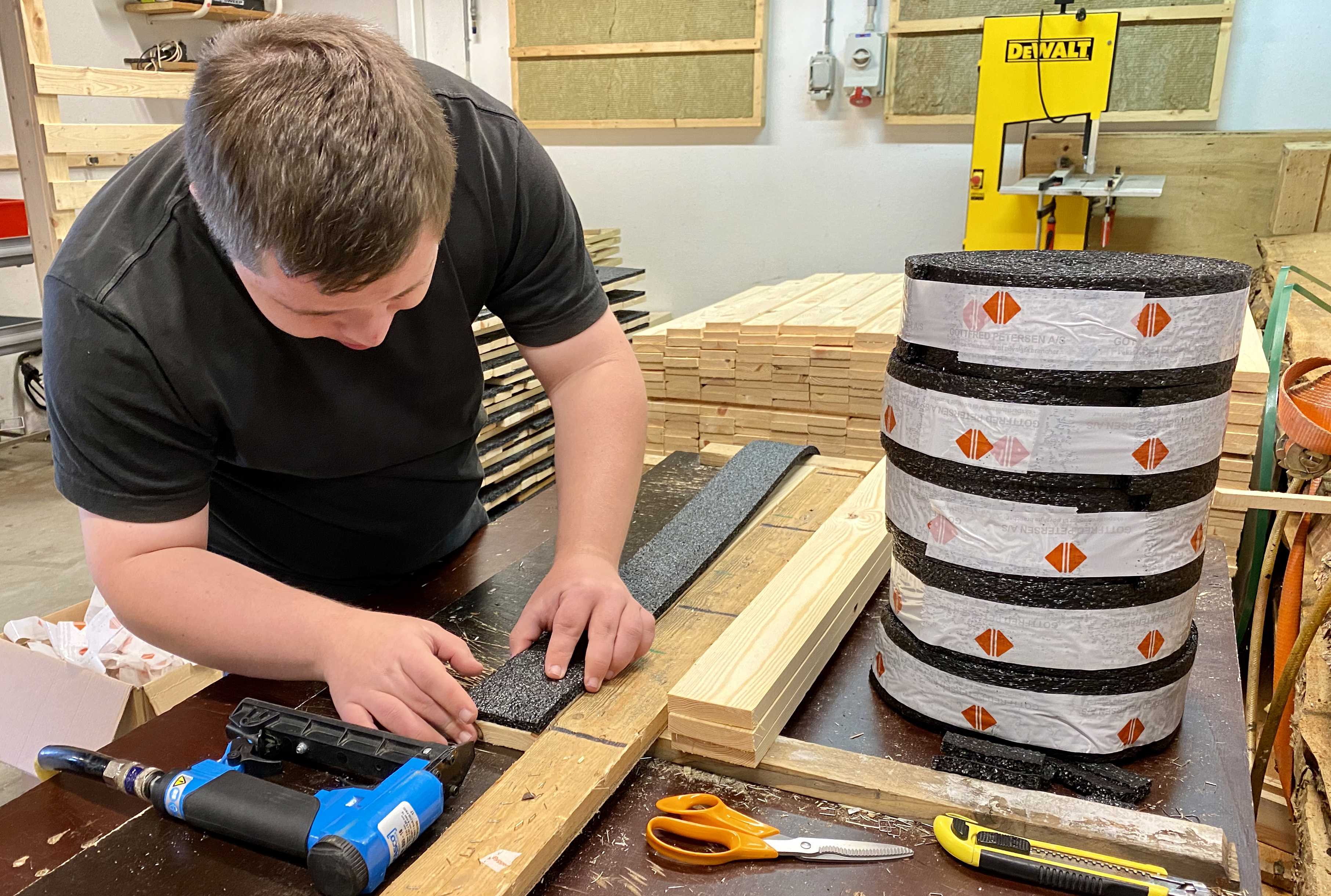 En borger er ved og sætte et bånd på en træliste, på bordet ligger 5 pakker bånd og tre trælister, en saks og en limpistol.