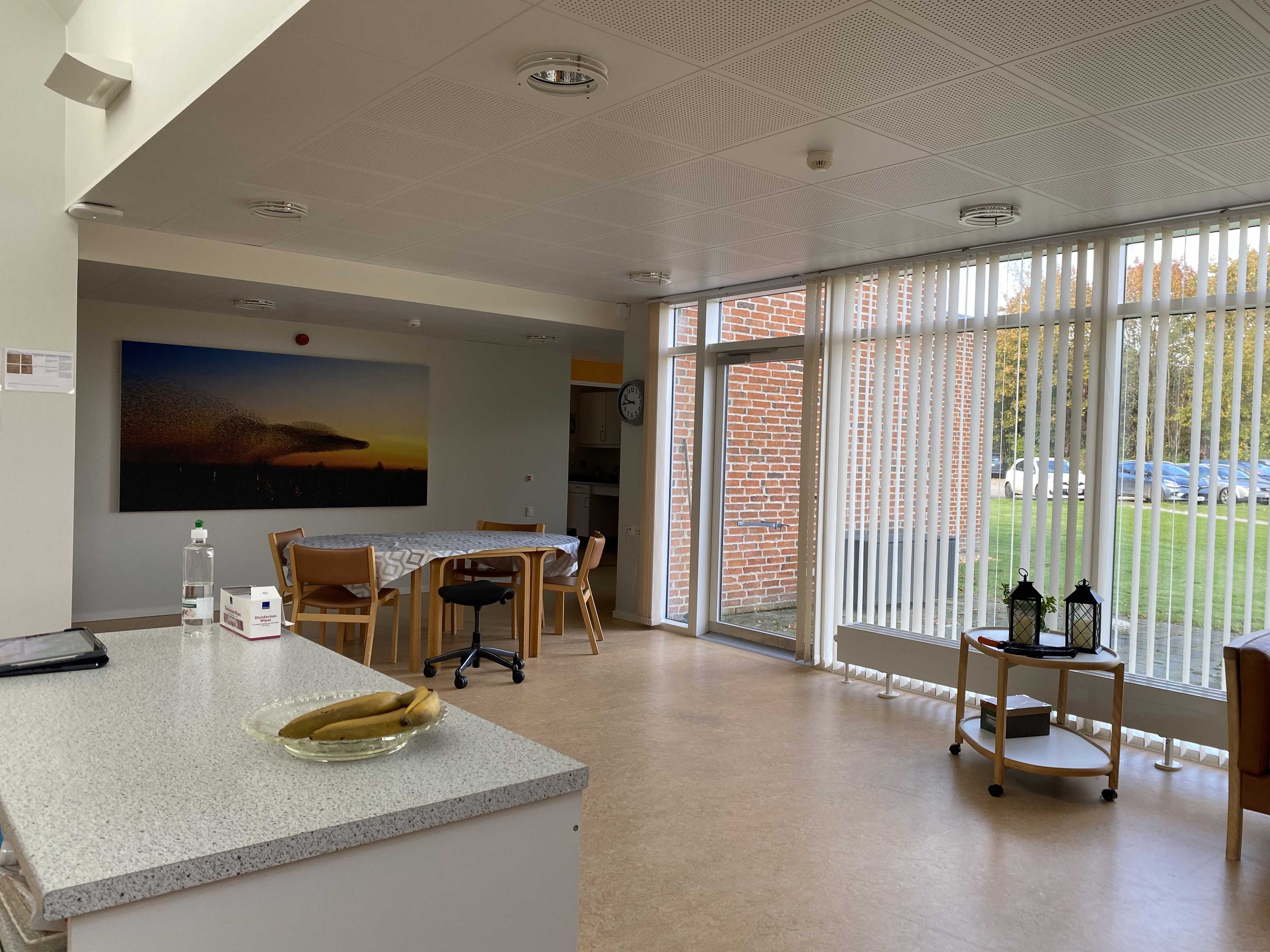 I opholdstuen er der et rundt bord med fire stole med rygløn og en stol med hjul. Henne ved det store vinduesparti er der et lille rullebord med nogle lanterner på.