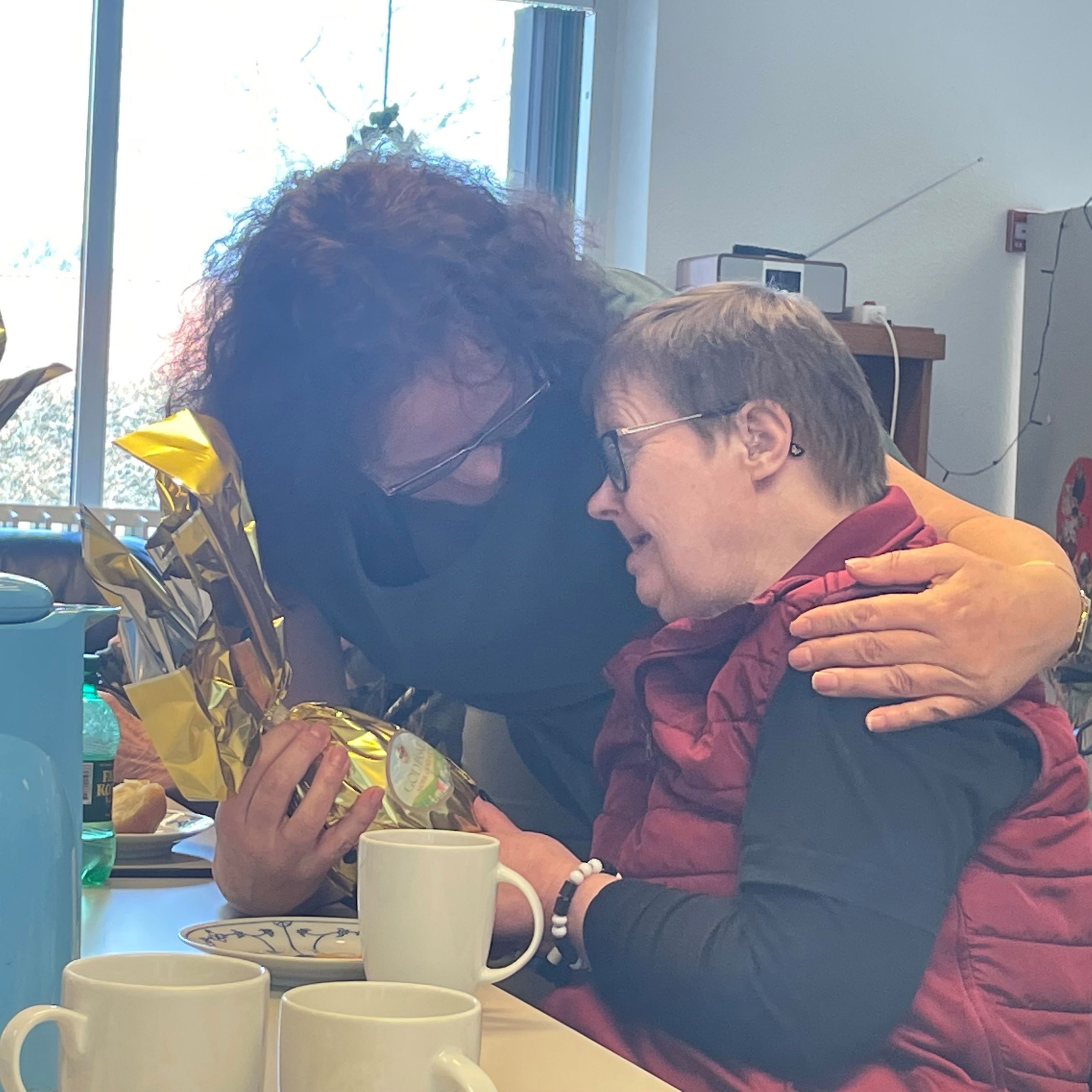 En borger får et påskeæg og et kram på bordet foran står der flere påskeæg og der sidder nogle borgere ved bordet