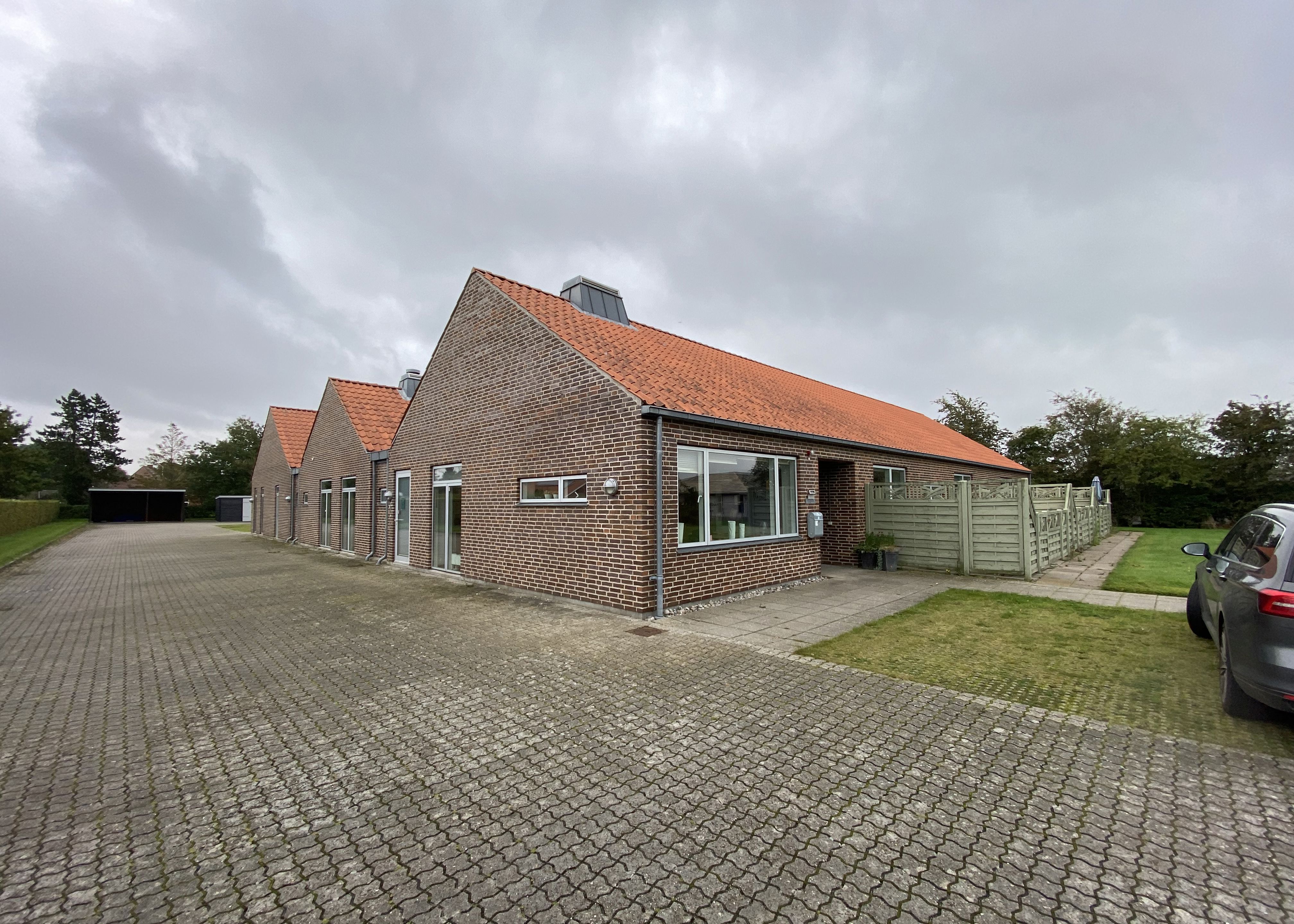 Ulriksallés bygninger forfra. Stor indkørsel med fliser der grænser på til bygningen der er lavet i røde mursten. Taget er af rødt tegl.