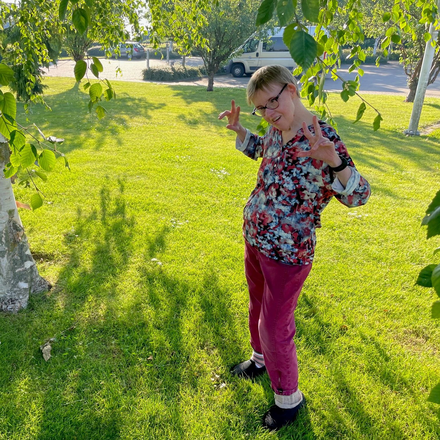 En borger står under et birketræ på den grønne græsplæne, i baggrunden ses parkeringspladsen med biler.