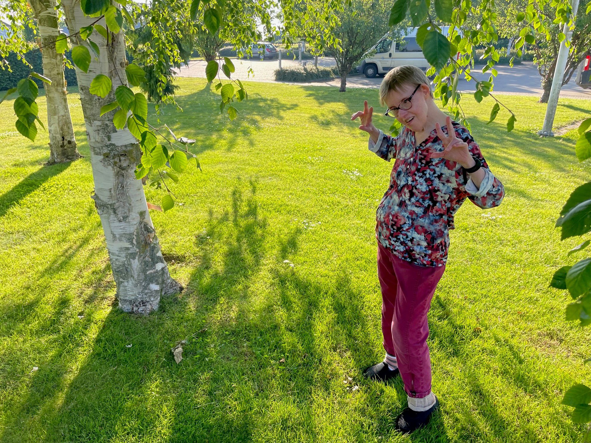 En borger står under et birketræ på den grønne græsplæne, i baggrunden ses parkeringspladsen med biler.