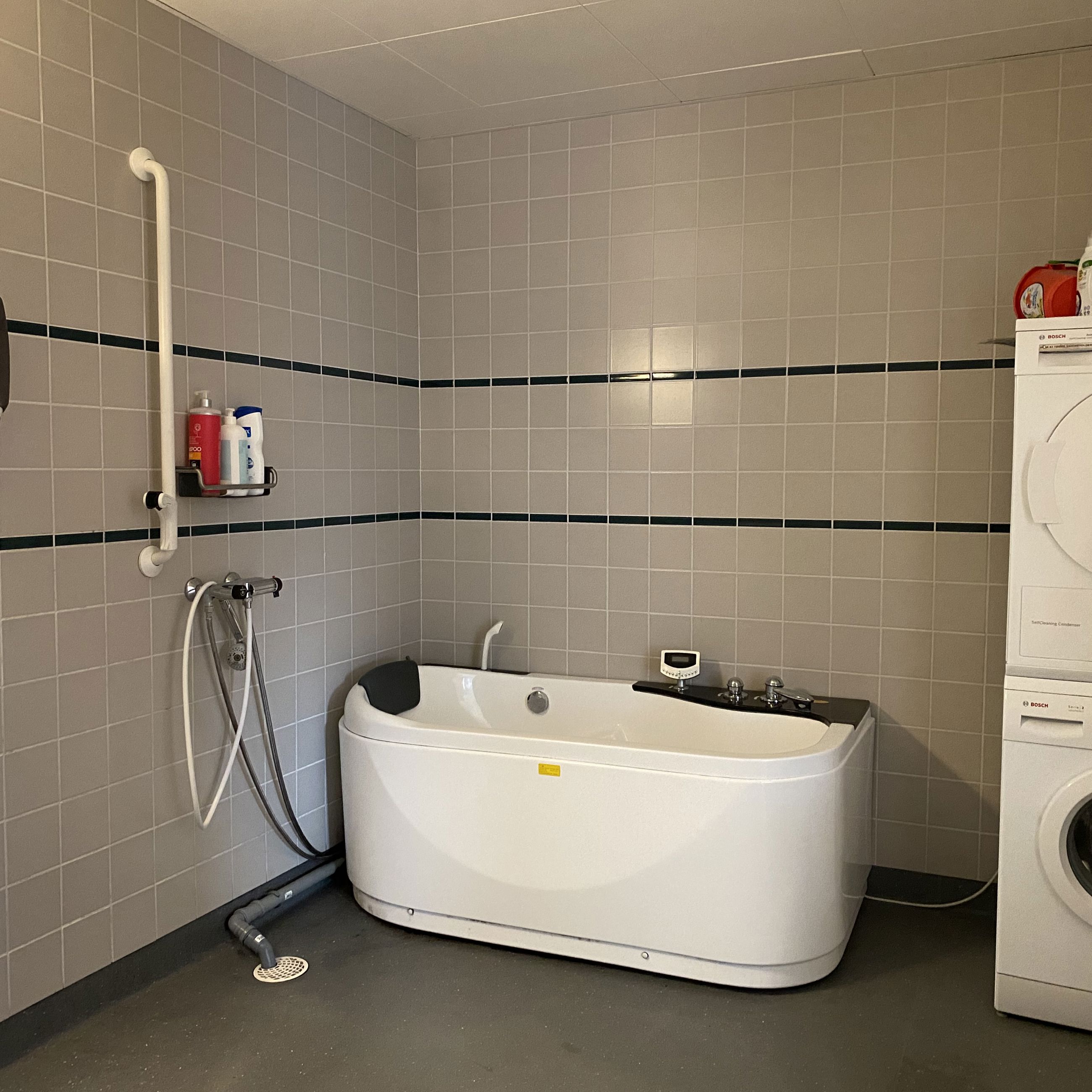 Badeværelset i en borgers lejlighed. Der er et spabad. I højre side af badeværelset er der en vaskemaskine og der står en tørretumbler ovenpå.