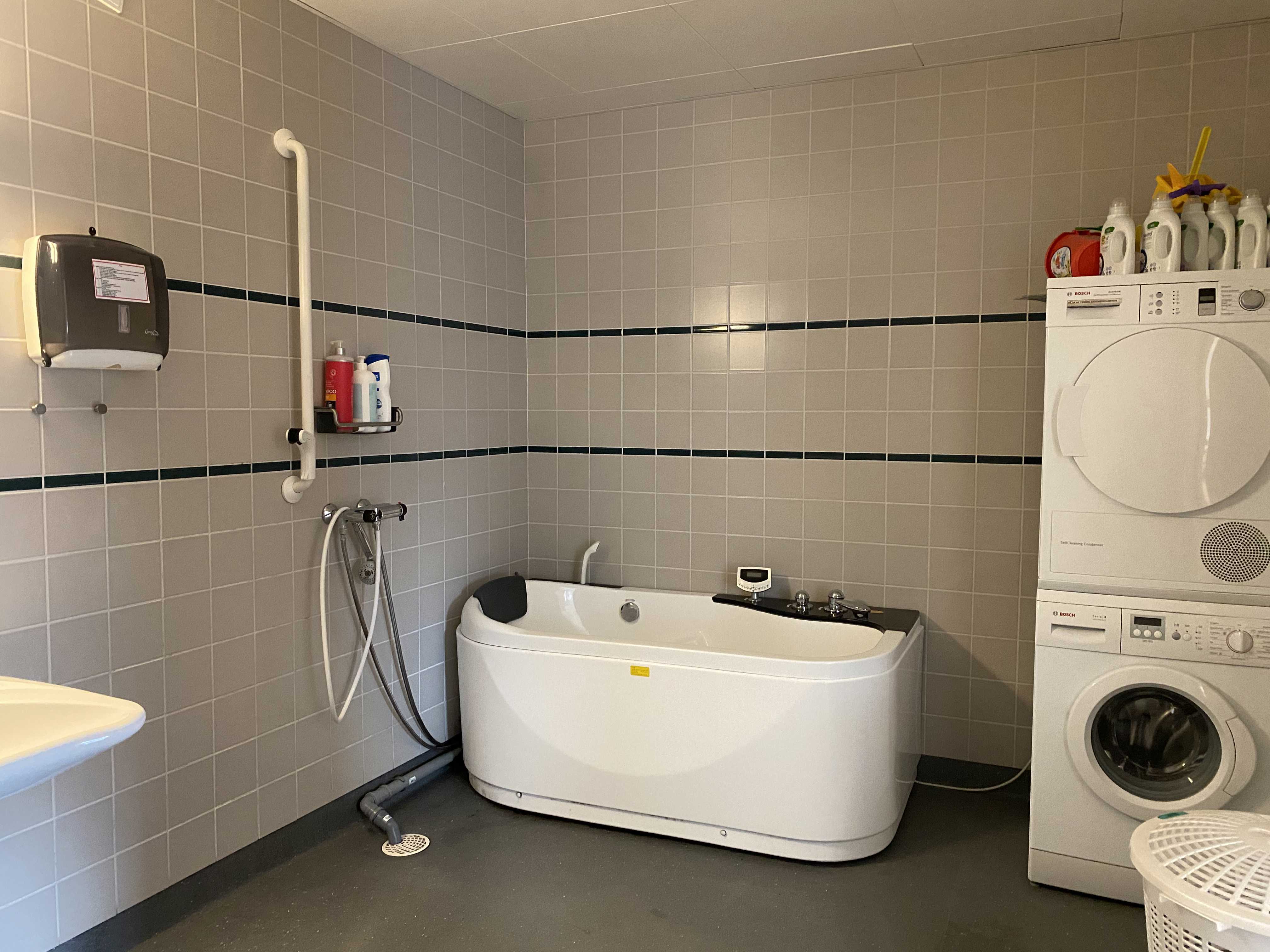 Badeværelset i en borgers lejlighed. Der er et spabad. I højre side af badeværelset er der en vaskemaskine og der står en tørretumbler ovenpå.