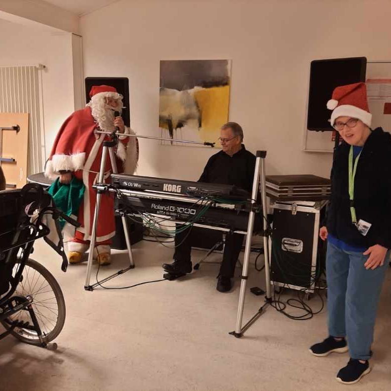 Julemanden står og giver et nummer, der sidder en mand ved et keyboard og spiller. I forgrunden står der en borger og danser.