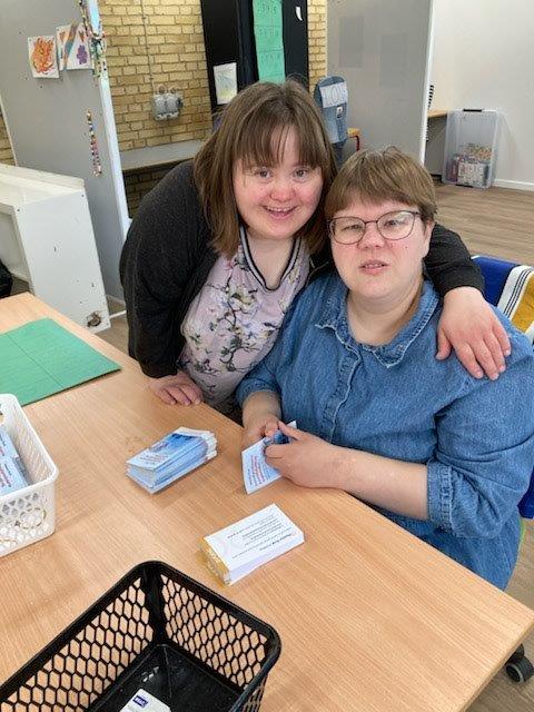 To borgere der holder om hinanden, mens de viser hvad de laver, de samler foldere. De ser begge glade og smilende ud.