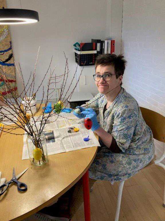 Borger sidder og maler påskeæg i forskellige farver, der står foran borgeren en vase med grene i. På disse grene skal de dekorede æg hænge på bagefter.