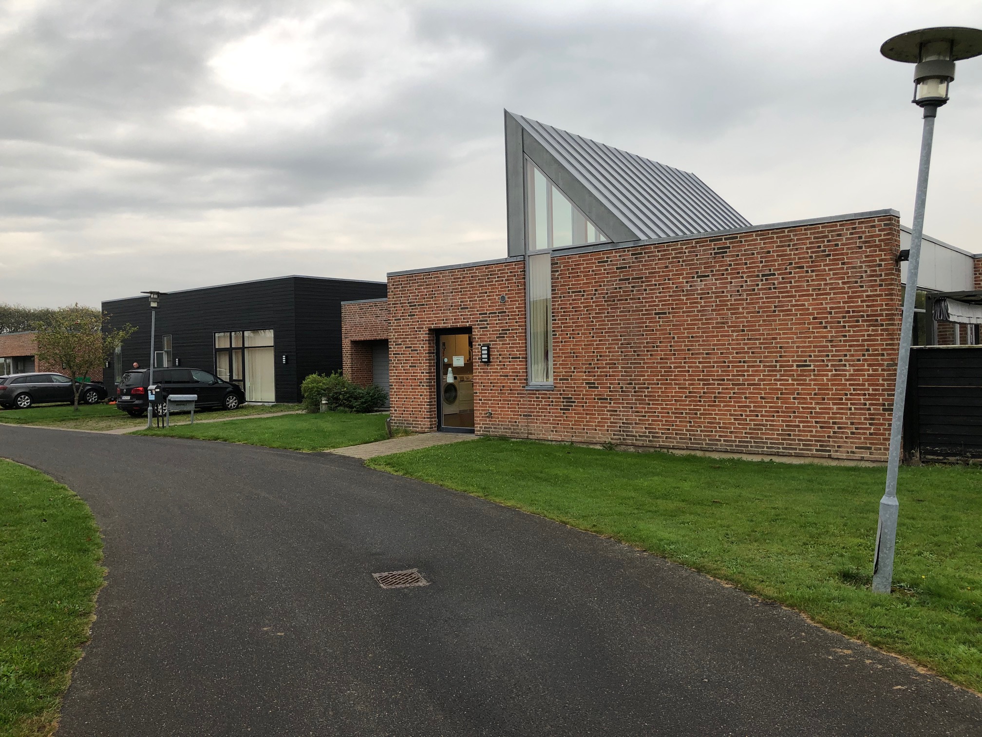 Æblevej 2 udefra. Bygninger er af røde mursten, og træ der er malet sort. Foran bygningerne er der en sti der fører ind til indgangen til Æblevej . Til højre i billedet står der en grå lygtepæl.